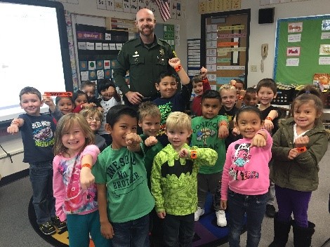 Photo of sheriff deputy standing with group of children in classroom